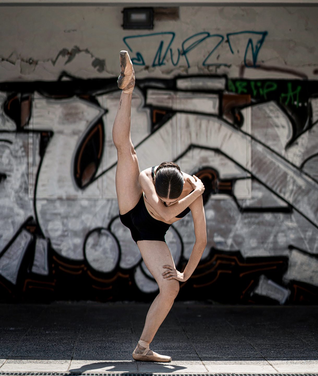 Bailarina realizando una postura muy flexible en la calle con graffiti de fondo balletthenewclassic Clases de Ballet Estiramientos y Flexibilidad para adultos en La Moraleja Alcobendas